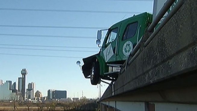 The cab of a big rig was left dangling over the edge of the Interstate 30/Trinity River bridge Thursday morning after a crash involving two freight trucks and an SUV.