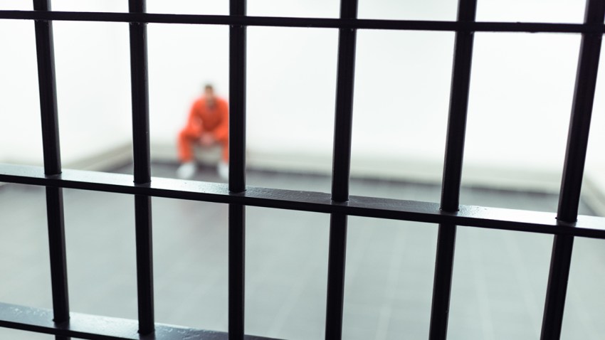 prisoner sitting on bench with prison bars on foreground