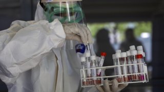 Person dressed in hazmat suit carrying a tray full of test tubes