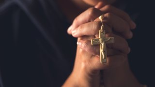A woman prays with clasped hands around a rosary.