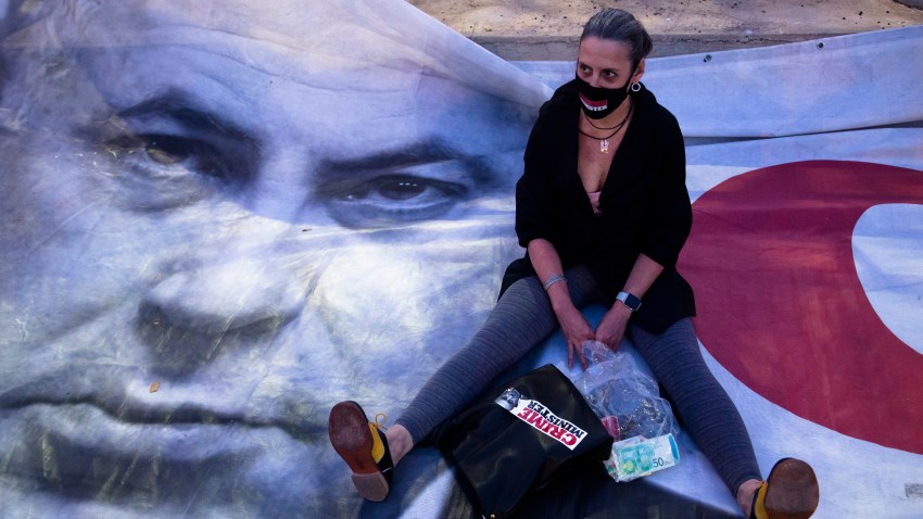 A woman sits on a placard showing Israeli Prime Minister Benjamin Netanyahu