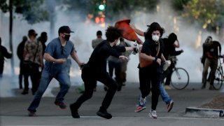Protesters run away as police shoot tear gas and flash grenades to disperse the crowd on Broadway near the Oakland Police Department during the fourth day of protests over George Floyd's death by the Minneapolis police in Oakland, Calif., on June 1, 2020.