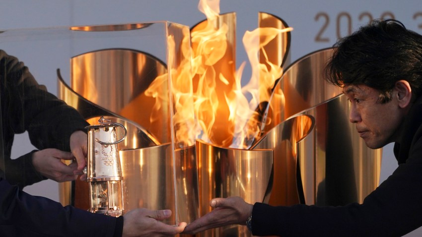 In this March 25, 2020, file, photo, officials light a lantern from the Olympic Flame at the end of a flame display ceremony in Iwaki, northern Japan.