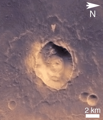 EMPTY_CAPTION"This picture of a heart-shaped feature in Arabia Terra was taken on 23 May 2010 by the CTX camera on the MRO spacecraft. A small impact crater near the tip of the heart is responsible for the formation of the bright, heart-shaped feature. When the impact occurred, darker material on the surface was blown away, and brighter material beneath it was revealed. Some of this brighter material appears to have flowed further downslope to form the heart shape, as the small impact occurred on the ejecta blanket of a much larger impact crater." Released in 2011.