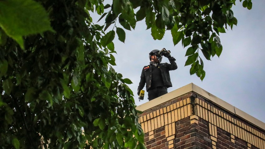 Obediah, a member of a neighborhood watch that started after the death of George Floyd in police custody sparked unrest, looks out from the roof of his home with binoculars, Tuesday June 2, 2020, in Minneapolis, Minn. A week of civil unrest has led some Minneapolis residents near the epicenter of the violence to take steps to protect their homes and neighborhoods.