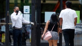 Amid concerns of the spread of COVID-19, a worker holds open the door for shoppers to enter the North Park Mall in Dallas, Saturday, May 2, 2020. Texas charged into its first weekend of re-opening the economy with residents allowed to go back to malls, restaurants, movie theaters and retail stores in limited numbers.