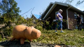 A toy sits on a log as a woman moves branches from a fallen tree to the curb, Friday, Aug. 14, 2020, in Cedar Rapids, Iowa. The storm that struck Monday morning left tens of thousands of Iowans without power as of Friday morning.