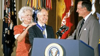 American First Lady Barbara Bush (1925 - 2018) fastens the Presidential Medal of Freedom around the neck of National Security Advisor Brent Scowcroft as he shakes hands with US President George HW Bush (1924 - 2018) during a ceremony in the White House's East Room, Washington DC, July 3, 1991.