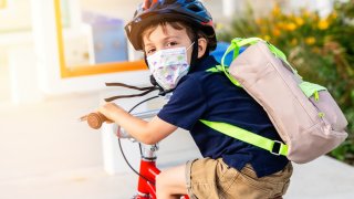 Little boy riding a bicycle wearing a protective mask.