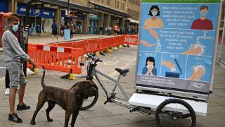 A man wearing a protective face mask restrains his dog beside a promotion funded by Calderdale Council, an ad bike display advising people on how to slow the spread of the coronavirus, in Halifax in northern England on August 9, 2020, as local lockdown restrictions are reimposed due to a spike in cases of the novel coronavirus in the town.