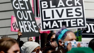 Protesters hold banners reading "Get Out Here" and "Black Lives Matter" during a demonstration led by the NAACP