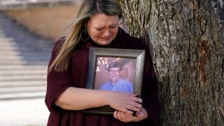 Katie Riggs Maxwell begins to cry as she hugs a portrait of her father Mark Riggs while posing for a photo, Wednesday, Dec. 16, 2020, on the campus of Abilene Christian University in Abilene, Texas. Mark Riggs, who was a professor at the school, passed away last Monday of COVID-19.