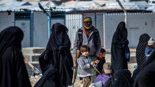 A member of Kurdish internal security stands guard as Women lead children ahead of departure during the release of another group of Syrian families from the Kurdish-run al-Hol camp which holds suspected relatives of Islamic State (IS) group fighters, in Hasakeh governorate in northeastern Syria, on January 28, 2021.