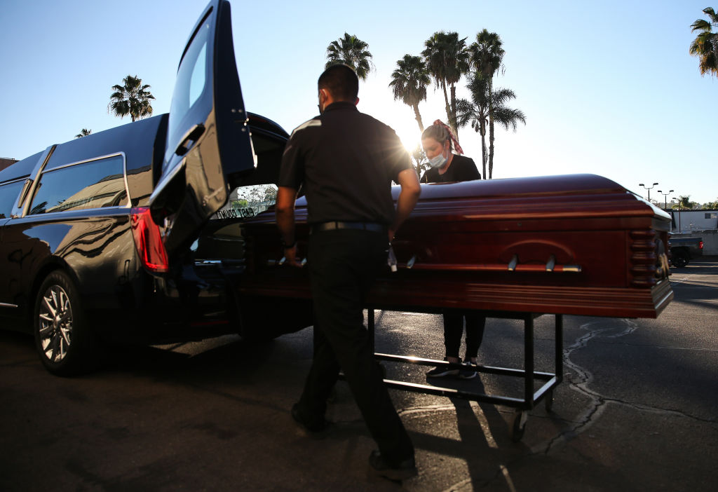 File Image: Embalmer and funeral director Kristy Oliver (R) and funeral attendant Sam Deras load the casket of a person who died after contracting COVID-19 into a hearse at East County Mortuary on January 15, 2020 in El Cajon, California. The mortuary on average was handling about 50 decedents per month but owner Robert Zakar believes they may process closer to 100 in January as California continues to see a spike in coronavirus deaths. The mortuary holds the bodies of those who pass away due to COVID-19 for a minimum of three days before they are processed along with various other COVID-related safety measures.