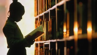 Girl 6-8 looking at a book next to a library shelf