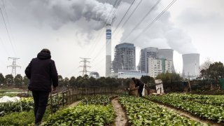 People tend to vegetables growing in a field as emission rises from cooling towers at a coal-fired power station in Tongling, Anhui province, China, on Wednesday, Jan. 16, 2019.