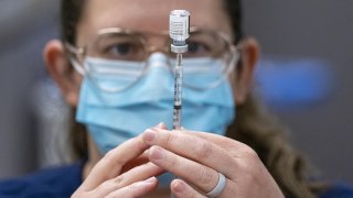 A healthcare worker wearing a protective mask fills a syringe with a dose of the Pfizer-BioNTech Covid-19 vaccine at a large scale vaccination site in Sacramento, California, Feb. 4, 2021.