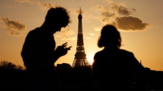 A couple, one checking his smartphone, enjoy the view of the Eiffel Tower at sunset in Paris on February 23, 2021.