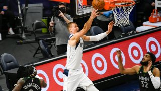 Dallas Mavericks center Kristaps Porzingis, center, releases a shot as Minnesota Timberwolves forward Jarred Vanderbilt (8) and center Karl-Anthony Towns (32) watch during the first half of an NBA basketball game Wednesday, March 24, 2021, in Minneapolis.