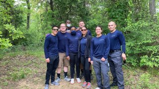 Eight police recruits in blue in a forest area.