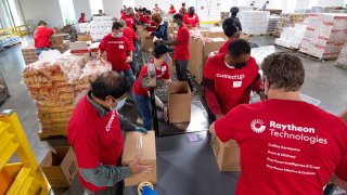 Multiple people in red Raytheon shirts pack up foods