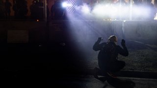 police shine lights on a demonstrator with raised hands during a protest outside the Brooklyn Center Police Department on in Brooklyn Center, Minn.
