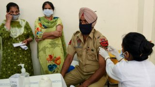 A medical worker inoculates a policeman with a dose of the Covishield coronavirus vaccine at a civil hospital in Amritsar on May 1, 2021 during the first day of India's vaccination drive to all adults.