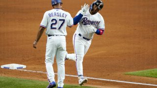 Texas Rangers third base coach Tony Beasley (27) celebrates with Willie Calhoun, right, as he runs home after hitting a solo home run off of New York Yankees starting pitcher Gerrit Cole in the fifth inning of a baseball game in Arlington, Texas, Monday, May 17, 2021.