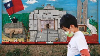 A kid wearing a mask walks past a mural with a Taiwan flag.