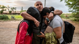 A migrant man embraces his wife and daughter after crossing the Rio Grande near the border between Mexico and the United States in Del Rio, Texas on May 16, 2021. Crossings in Del Rio have risen significantly this year with many coming to seek asylum from Venezuela.