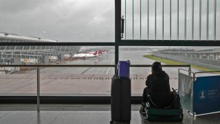 A passenger sits on her luggage watching passenger airplanes parked on the tarmac after all flights were canceled at Pudong International Airport in Shanghai, China