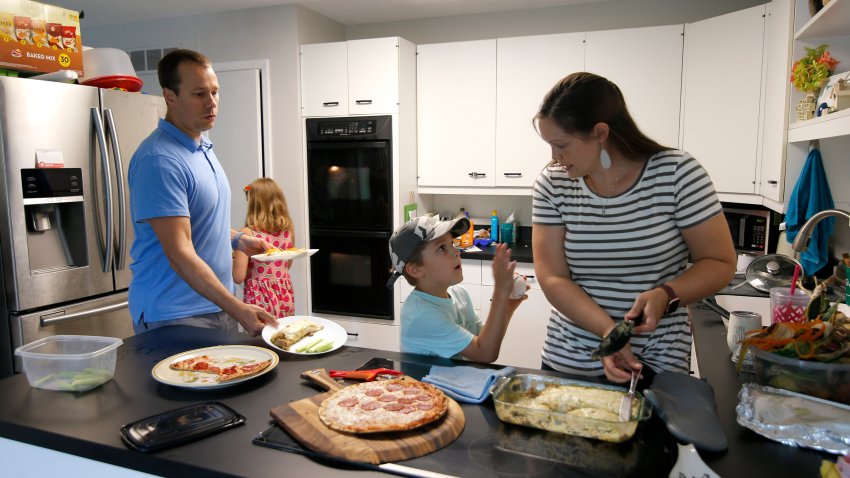 Chris and Kristen Umphlett prepare dinner with two of their four children, Kyria, 9, rear, and Derek 7, Wednesday, June 30, 2021, in their home in East Lansing, Mich. The Umphletts have fostered unaccompanied migrant children during the pandemic.