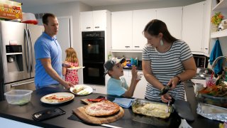 Chris and Kristen Umphlett prepare dinner with two of their four children, Kyria, 9, rear, and Derek 7, Wednesday, June 30, 2021, in their home in East Lansing, Mich. The Umphletts have fostered unaccompanied migrant children during the pandemic.