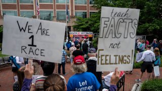 People hold up signs during a rally against "critical race theory" (CRT) being taught in schools at the Loudoun County Government center in Leesburg, Virginia on June 12, 2021.