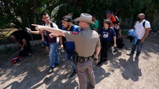 In this Wednesday, June 16, 2021, file photo, A Texas Department of Public Safety officer in Del Rio, Texas directs a group of migrants who crossed the border and turned themselves in.