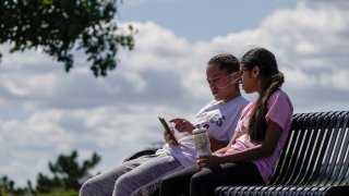 Savannah Brown and Glendy Stollberg use their phone in Kilbourn Reservoir Park
