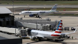 A JetBlue Airbus A320 taxis to a gate Wednesday, Oct. 26, 2016, after landing as an American Airlines jet is seen parked at its gate at Tampa International Airport in Tampa, Fla.