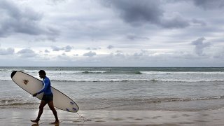 a surfer walks along the beach after surfing in Coffs Harbour, Australia