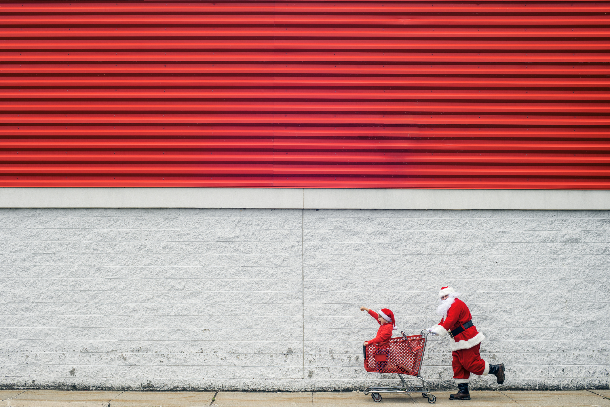 Santa Claus and child sitting in shopping cart rushing to get the best Christmas deals before the season