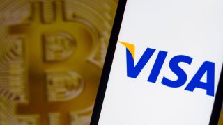 The Visa logo seen displayed on a smartphone with a bitcoin logo in the background.