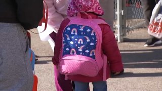 a little girl wearing a pink winter jacket with a pink and blue backpack