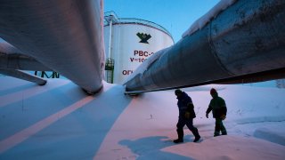 Employees pass beneath pipes leading to oil storage tanks at the central processing plant for oil and gas at the Salym Petroleum Development oil fields near the Bazhenov shale formation in Salym, Russia.