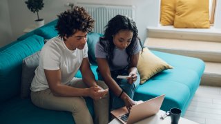 Young african american couple using a laptop and a credit card while managing their expenses at home and calculating their home budget. Online shopping. Checking accountancy and bills.