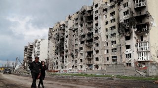 People walk along a street near residential buildings destroyed during Ukraine-Russia conflict in the southern port city of Mariupol, Ukraine April 22, 2022.