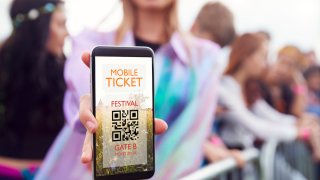 Close Up Of Woman Holding Mobile Phone Screen To Camera As She Arrives At Entrance To Music Festival