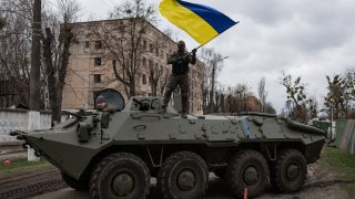 A Ukrainian soldier waves the national flag while standing on top of an armoured personnel carrier (APC) on April 8, 2022 in Hostomel, Ukraine.