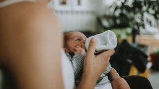 Midsection Of Woman Feeding Milk To Newborn Son At Home