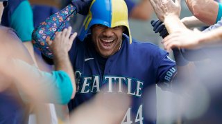 Seattle Mariners' Julio Rodriguez wears a helmet as he is greeted in the dugout after his three-run home run against the Texas Rangers during the seventh inning of a baseball game Wednesday, July 27, 2022, in Seattle.