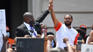 FILE – Attorney Benjamin Crump, left, holds up the hand of Kenneth Walker during a rally on the steps of the Kentucky State Capitol in Frankfort, Ky., on June 25, 2020.