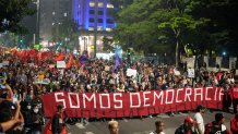 Demonstrators march holding a banner that reads in Portuguese "We are Democracy"